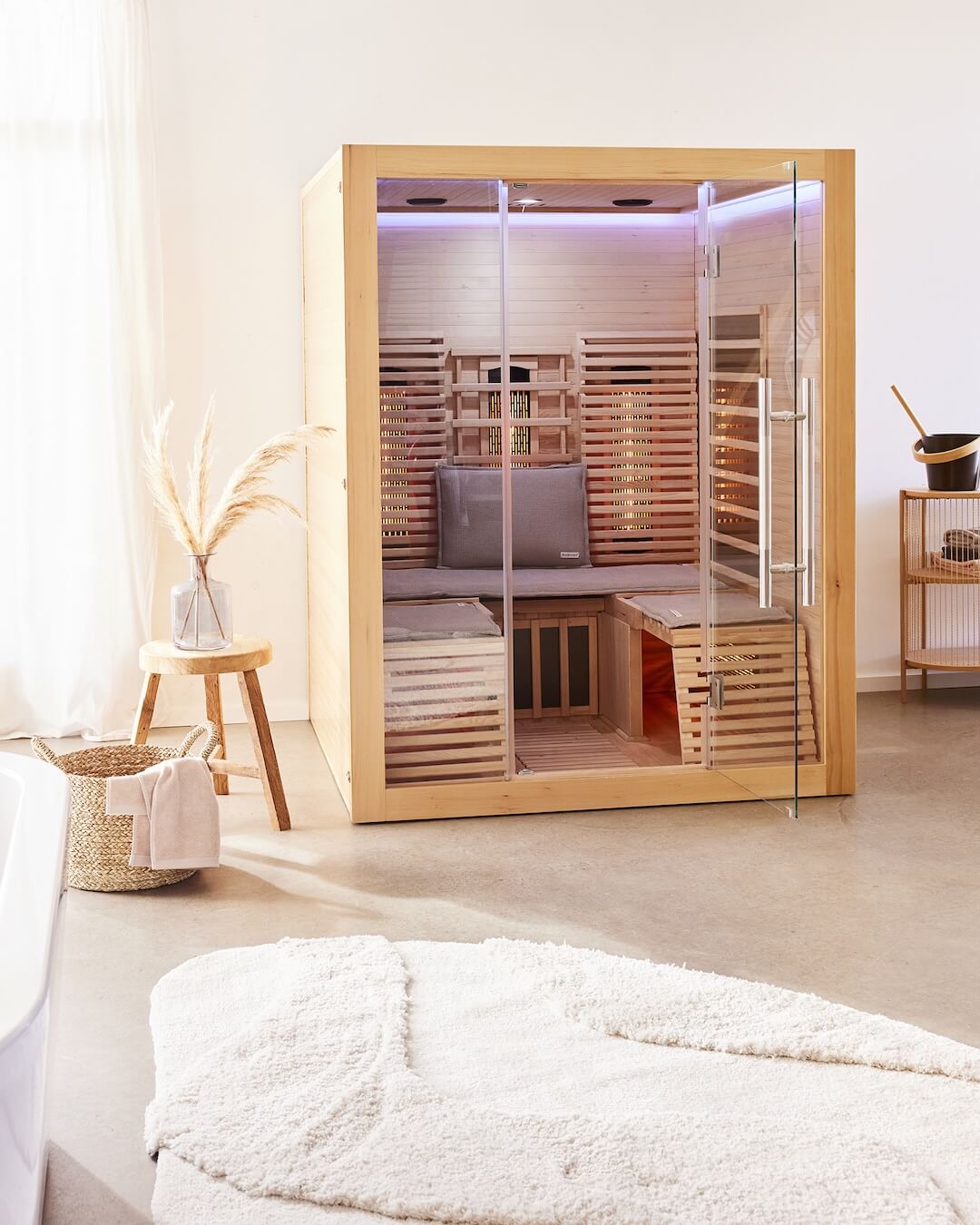 Freistehende Infrarotsauna-Kabine in der eine Saunauflage short, zwei Saunasitzkissen und ein Kopfkissen dekoriert sind.