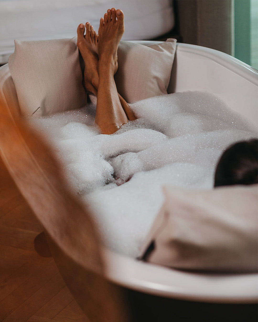 Eine Frau legt entspannt beim Baden die Füsse auf ein Badesofa Fusskissen.