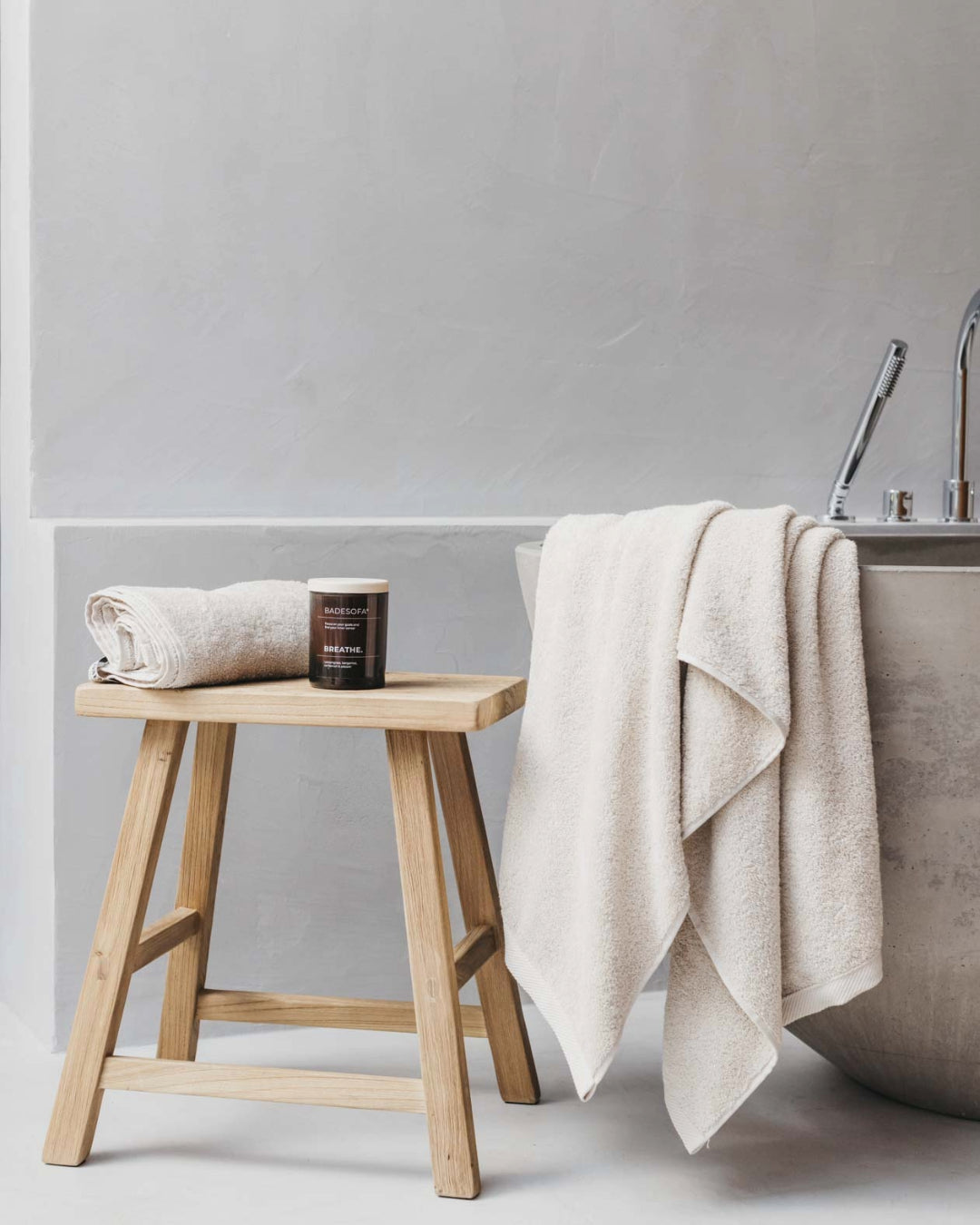 Stilleben neben einer Badewanne aus Holzhocker Frottee Handtüchern und einer Duftkerze.